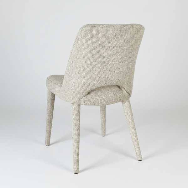 An upholstered dining chair with a textured light beige fabric and tapered legs, shown from a three-quarters angle on a light gray studio background.