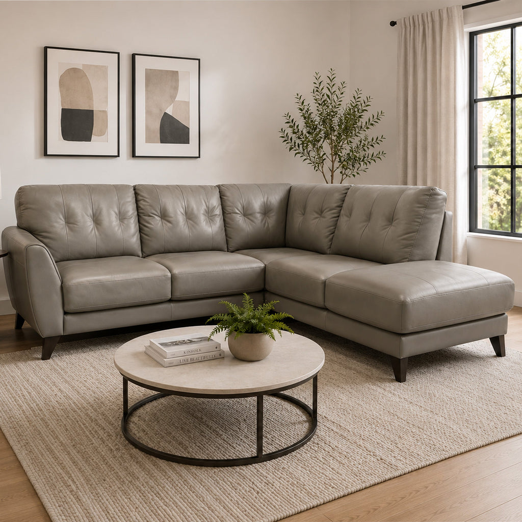 Gray sectional sofa in a living room with a round coffee table, plant, and abstract art on the wall.