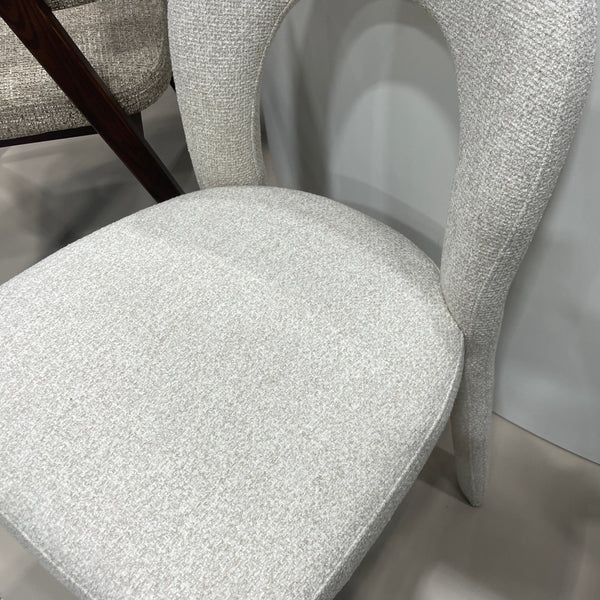 A close-up of a modern upholstered chair with a curved, loop-like backrest and a rounded seat cushion, covered in light gray textured fabric.