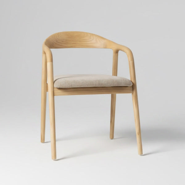 A modern wooden dining chair with a curved backrest, integrated armrests, and a light beige upholstered seat cushion, shown against a neutral light gray background.