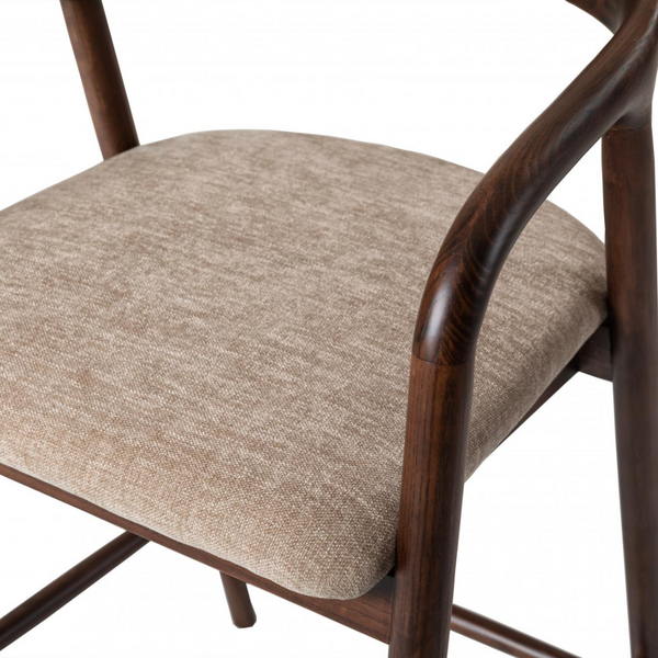 A close-up of a modern armchair with a curved dark brown wooden frame and a textured beige fabric seat cushion, shown against a plain white background.