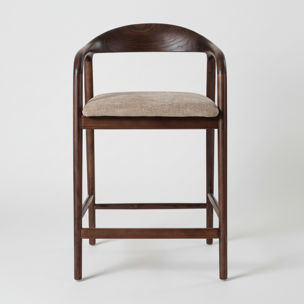A modern bar stool with a curved dark brown wooden frame, a light beige textured fabric seat cushion, and a footrest, shown against a plain white background.