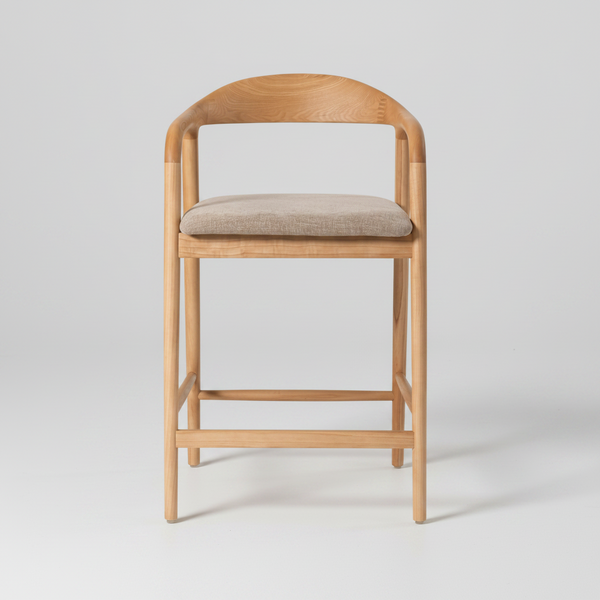 A modern wooden bar stool with a curved backrest, light oak frame, and a beige textured fabric seat cushion, shown against a plain white background.