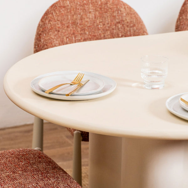 Round beige table with plates and gold forks on a wooden floor.