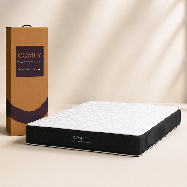 A COMFY mattress in a box shown next to its tall cardboard packaging box on a warm beige studio background.