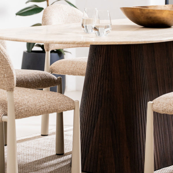 Dining table with dark ribbed pedestal base and beige upholstered armchair