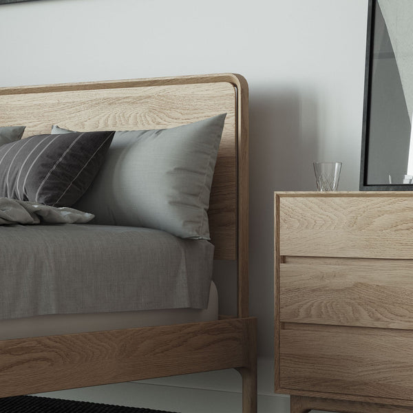 Light oak bed frame with curved headboard, gray bedding, and a bedside dresser