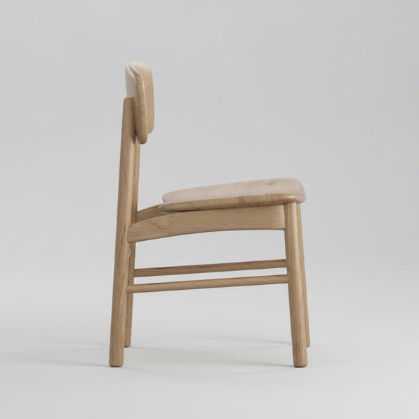 Light wood dining chair, side view with curved backrest and smooth arm support