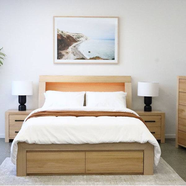 Wooden bed frame with headboard and white bedding, storage drawers underneath