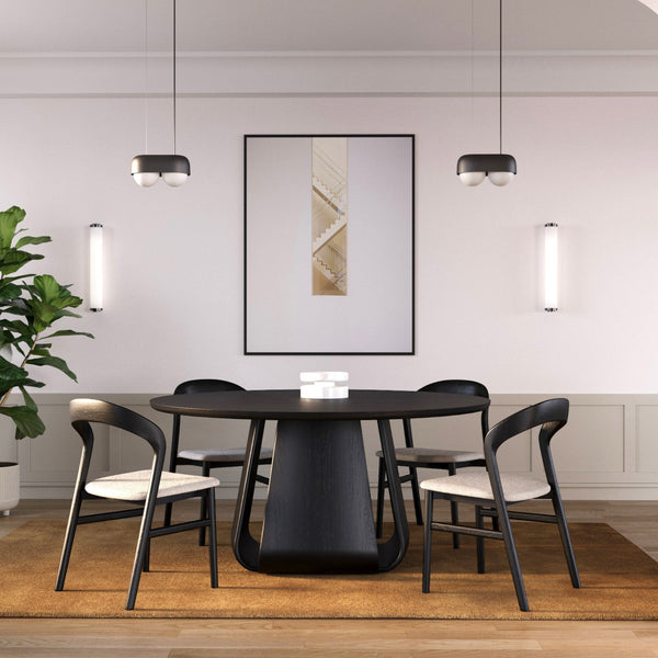 A modern dining setting featuring a round oak dining table with a central Pedestal base and willow chairs arranged around it, in a room with a light grey wall color and a decorative picture on the wall.