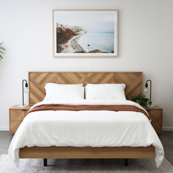 Queen bed with geometric wood headboard, white duvet, two pillows, brown bed runner
