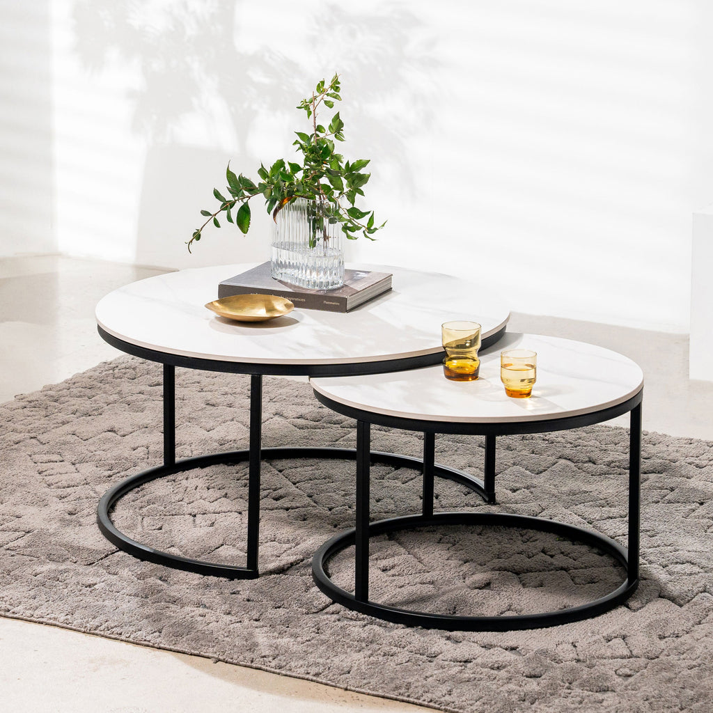 Two round nested tables with white marble-look tops, black frames, and open circular shelves