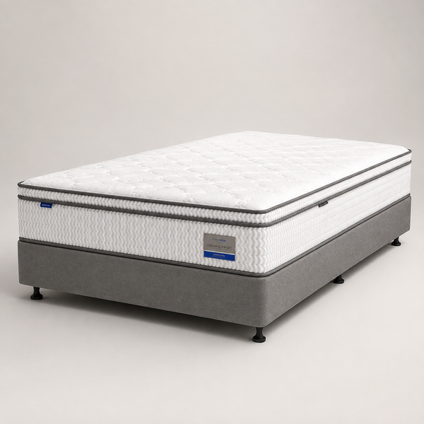 A mattress on a gray upholstered bed base, photographed in a clean studio setting against a light gray background.