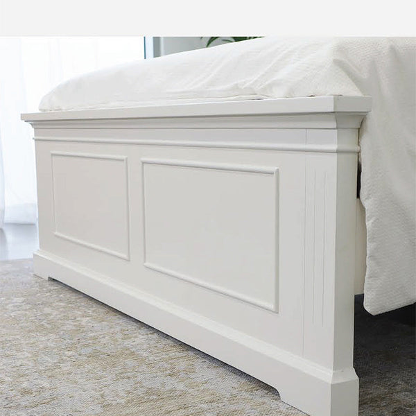White paneled footboard with inset rectangular panels and bed sheet